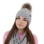 Caciula de dama gri deschis din lana merinos, tricotata cu model impletit si pompon decorativ.
